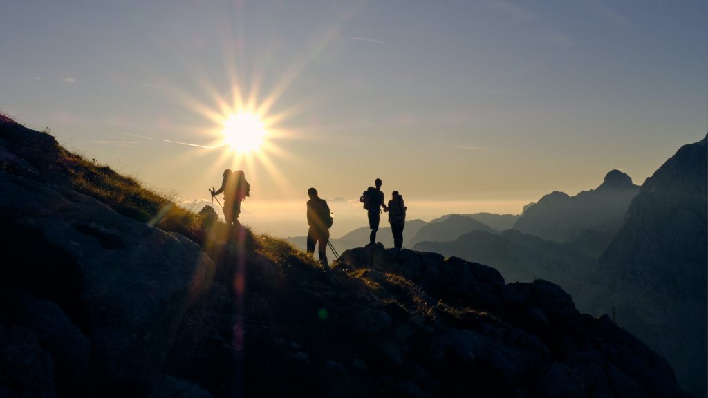 Landscape image of four silhouetted hikers on a mountain summit in the Rocky Mountains