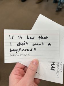 A hand holds index cards. In black ink, text says, "Is it bad that I don't want a boyfriend? informational".
