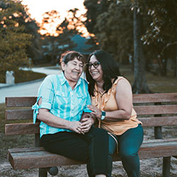 Two older adults share a park bench holding hands while laughing.