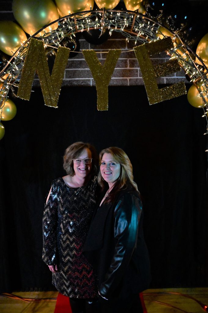Angie Bertrand and Jackie Sievers stand underneath a sign that reads NYE