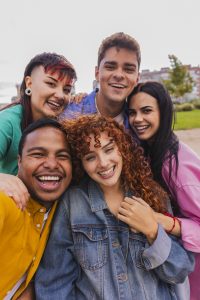 close-up of five diverse college friends smiling while taking a selfie outdoors on a sunny day.