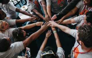 A group of people place their hands in a circle to convey teamwork.