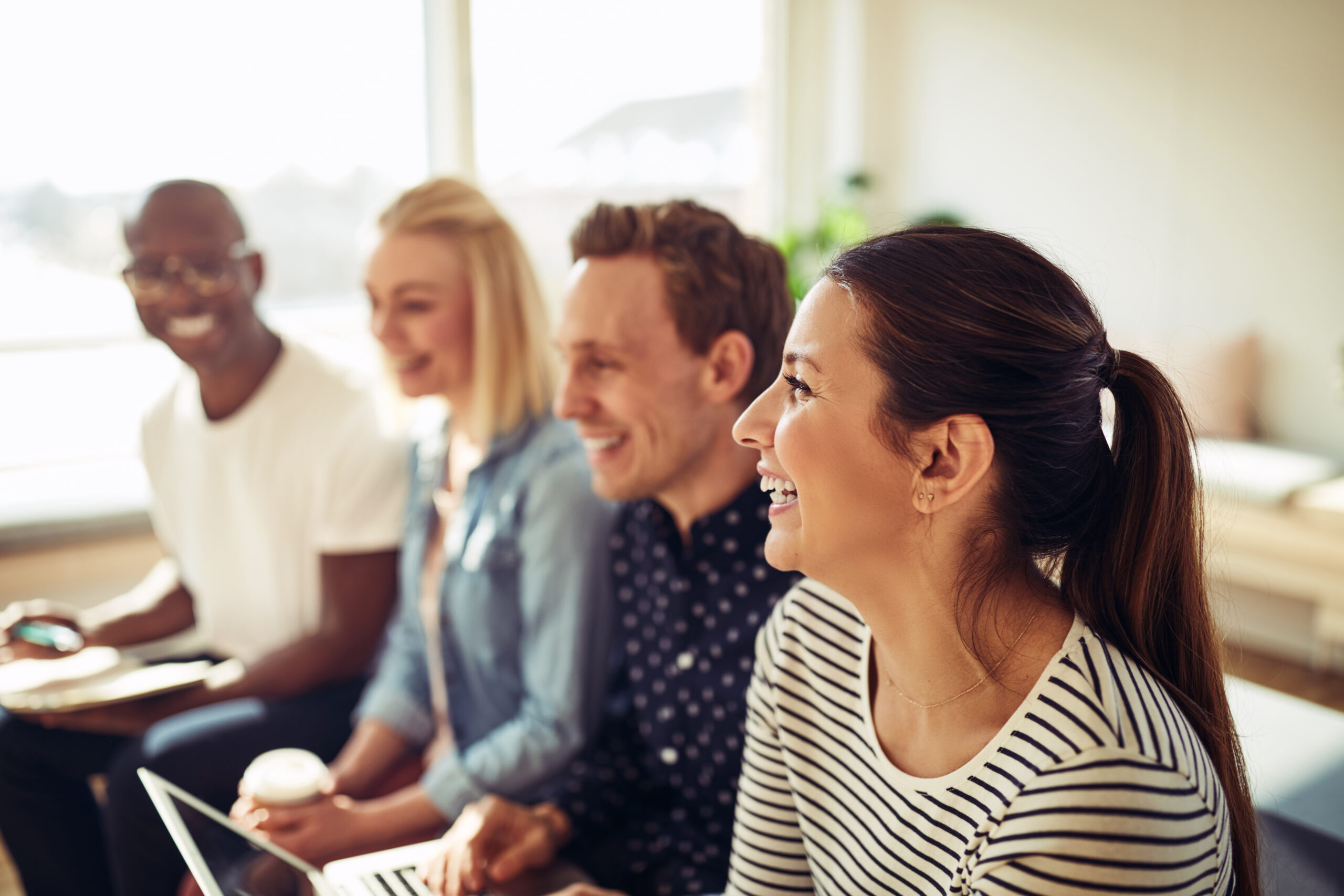 Diverse group of businesspeople laughing while sitting in a row together during a presentation in an office