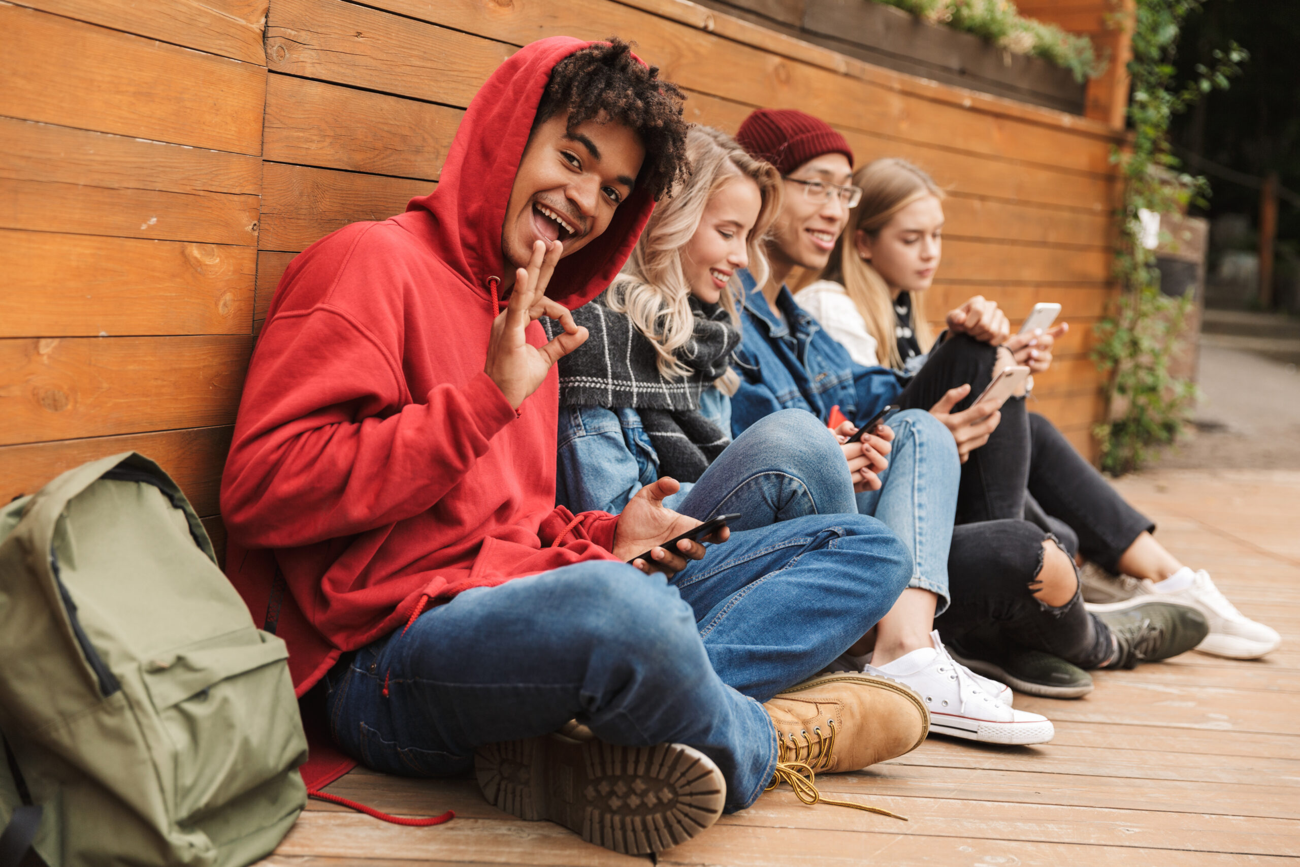 Happy multhietnic friends students hanging out together outdoors, using mobile phones