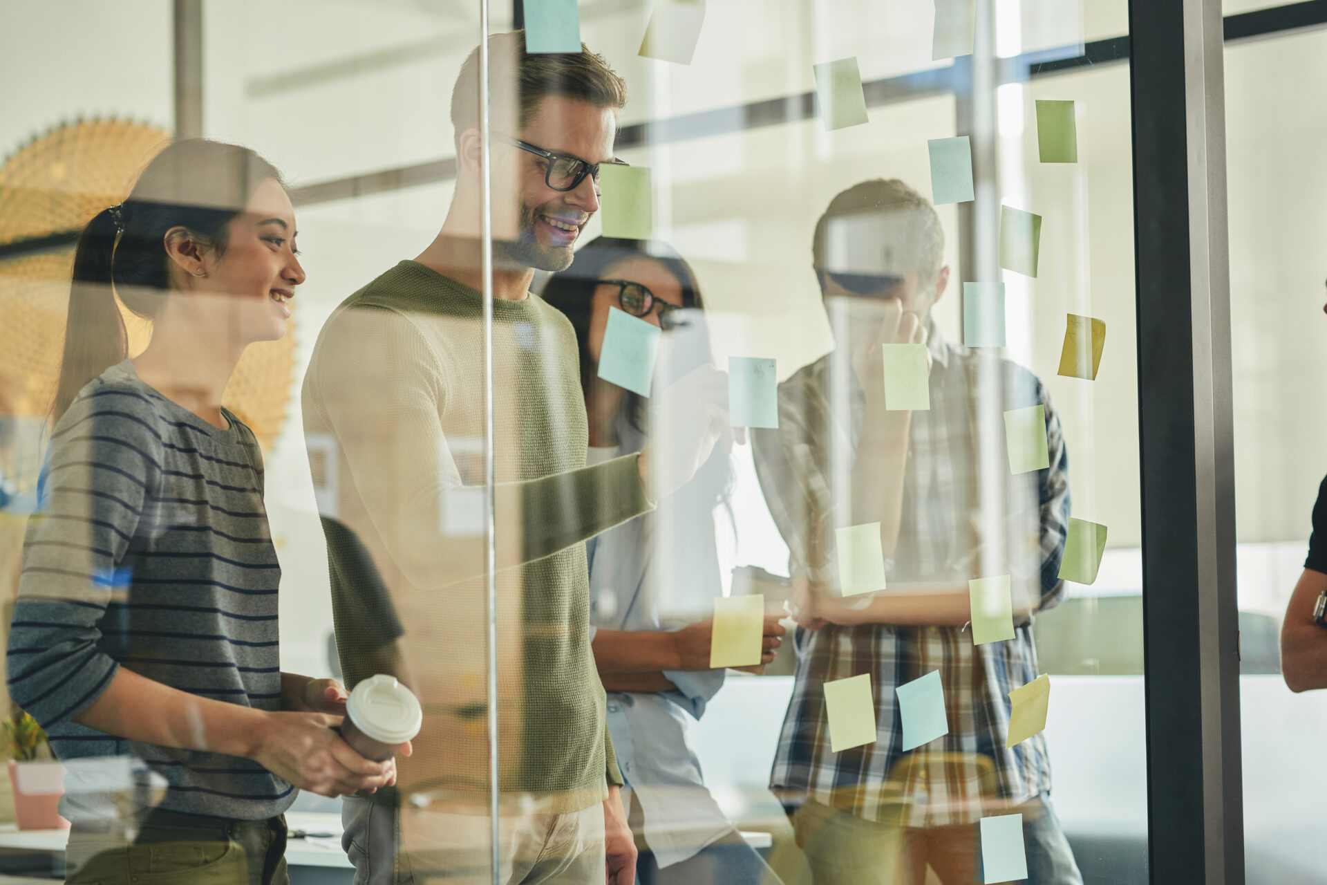 Group photo of young industrious people brainstorming ideas and putting sticky notes on glass window